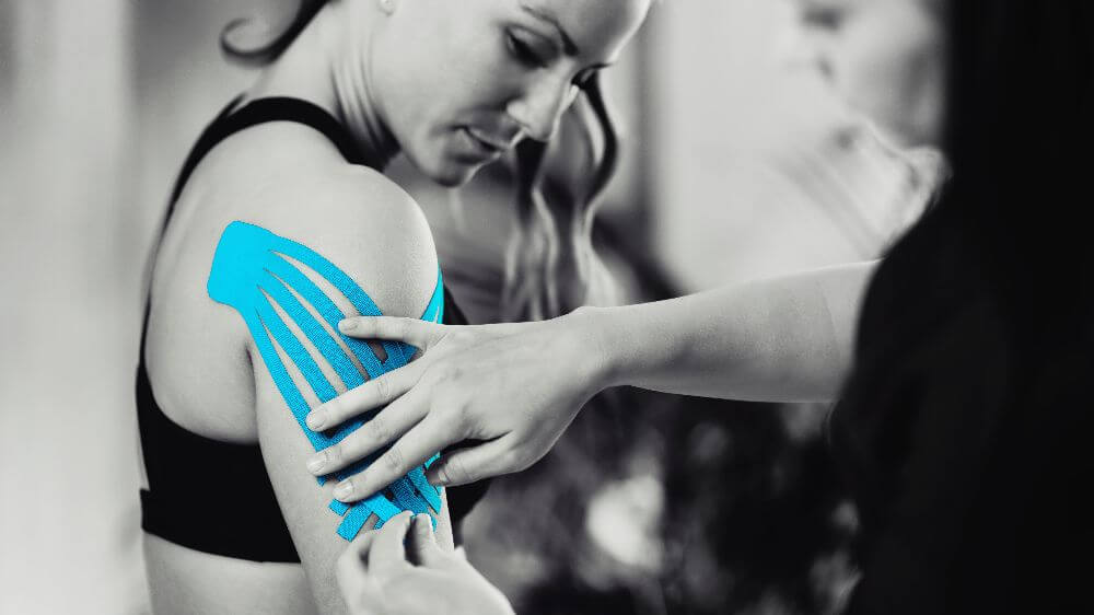 physical therapist putting kinesio tape on shoulder
